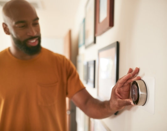 Man adjusting thermostat on wall in hallway