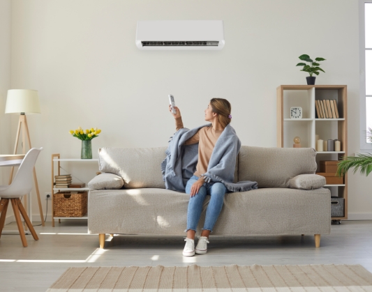 Woman sitting on couch and adjusting air conditioning system with remote