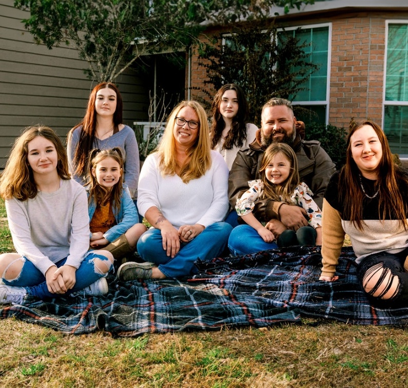 Joe sitting in his front yard with his wife and six kids