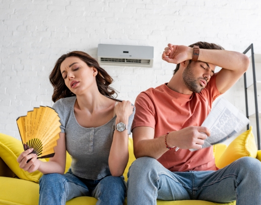 Man and woman sitting on couch and fanning themselves